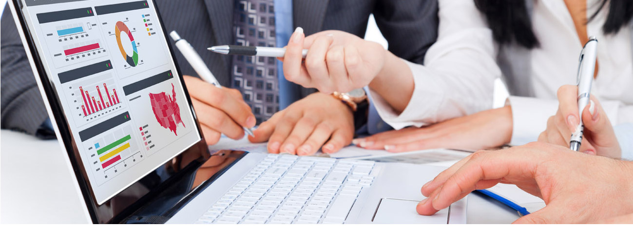 People analyzing charts and graphs on a laptop while discussing and gesturing with pens.