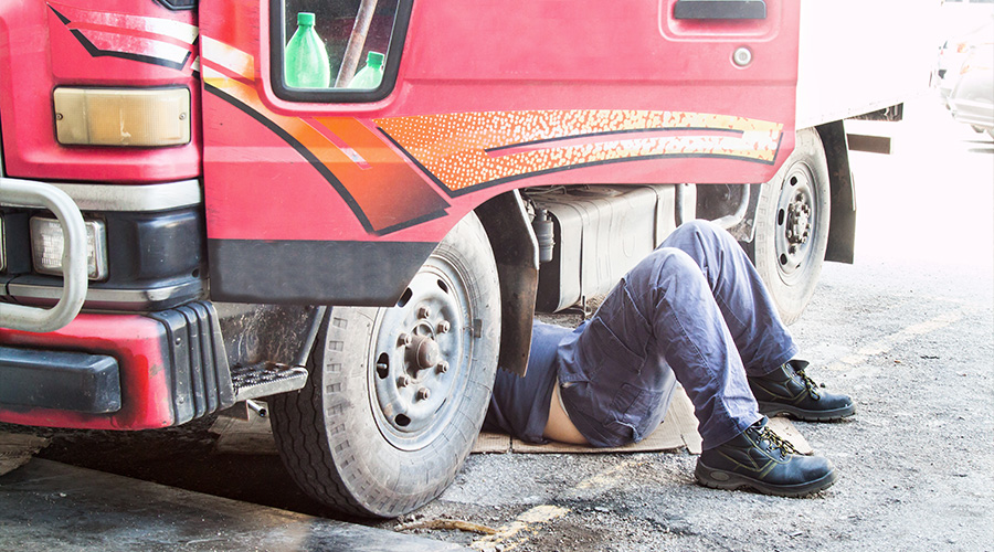 Mechanic under truck repairing the engine with problem. Concept image of “3 Major Issues In Heavy Duty Truck Repair (And How To Resolve Them)” | Consolidated Truck Parts & Service in Alexandria, LA.