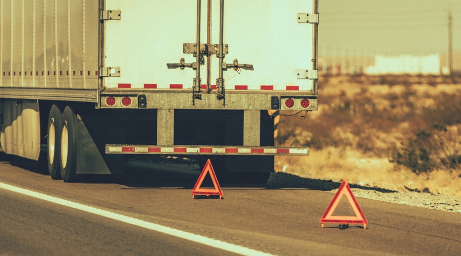 Emergency roadside assistance in Monroe, LA with Consolidated Truck Parts & Service. Image of the back of a tractor-trailer that is on the side of the road due to break down with 2 triangle warning signs set up for oncoming traffic.
