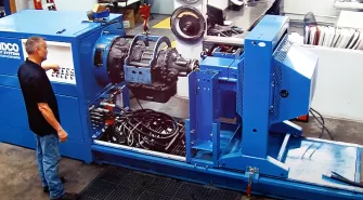 A person operates industrial machinery in a workshop, surrounded by various equipment and cables, as they specialize in truck repair services.