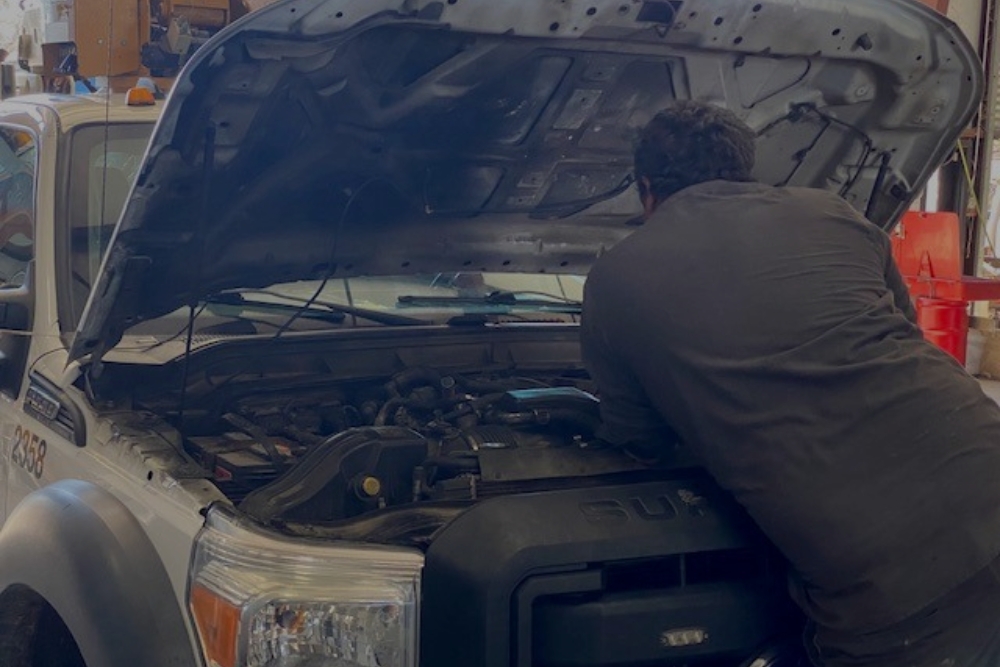 Technician working under the hood of a white truck inside a repair bay – Truck repair in Alexandria, LA at Consolidated Truck Parts & Service